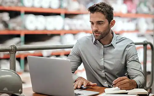 Warehouse manager taking notes and checking orders with a laptop